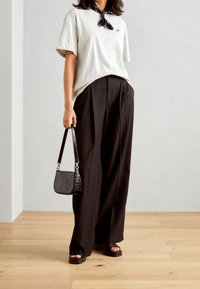 Szara bawełniana koszulka z małym czerwonym logo, zestawiona z czarnymi spodniami o szerokich nogawkach. W komplecie czarna torba o teksturowanym wykończeniu oraz płaskie sandały.