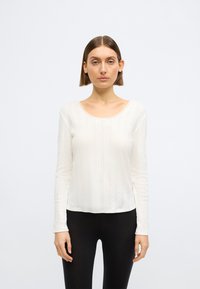 Άσπρο μακρυμάνικο τοπ με ριμπ υφή και στρογγυλή λαιμόκοψη με διακοσμητικό δαντέλα. Συνδυασμένο με μαύρο εφαρμοστό κολάν.