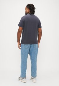 Σκούρο γκρι t-shirt με κοντά μανίκια, συνδυασμένο με ανοιχτό μπλε φαρδιά τζιν παντελόνια. Το σύνολο χαρακτηρίζεται από άνετη εφαρμογή και κλασικό σχέδιο.