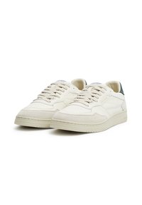 White sneakers with a textured upper, smooth leather and suede materials, round toe, and contrasting dark green heel accent.