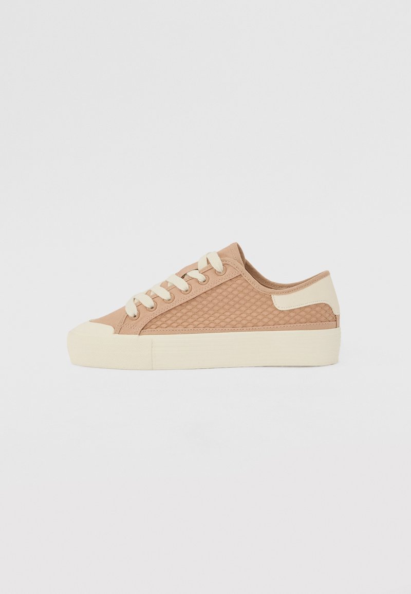 Sneaker beige con lati in rete, punta rotonda e suola in gomma crema. Presenta lacci piatti e dettagli di cucitura laterale per il supporto.