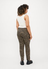 Dámské skinny kalhoty s leopardím potiskem v černé a béžové barvě, kombinované s bílým tílkem a černými robustními platformovými botami.