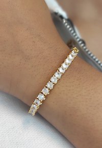 Gouden armband met heldere, ronde edelstenen, gezet in een lineair ontwerp. Glad oppervlak met een delicate sluiting, gedragen om een pols.