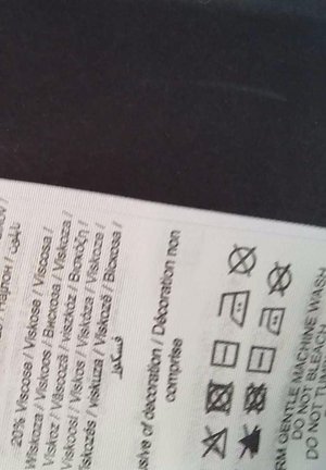 Onderhoudslabel op stof, met wassymbolen en instructies, gedrukt in zwart op een witte achtergrond. Tekst bevat details over de vezelsamenstelling.