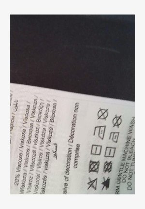 Onderhoudslabel op stof, met wassymbolen en instructies, gedrukt in zwart op een witte achtergrond. Tekst bevat details over de vezelsamenstelling.