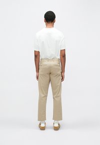White T-shirt made of cotton, paired with beige straight-leg pants. Notable details include back pockets and light brown shoes.