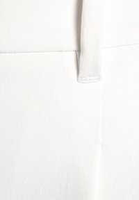Primo piano di un tessuto di cotone bianco, caratterizzato da una trama liscia e dettagli di cucitura sottili, con una cucitura verticale e un legaccio in tessuto.