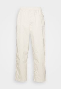 Ljusa beige byxor med elastisk midja och vida ben. Tillverkade av slätt tyg. Har en liten vit logotyp på övre benet.