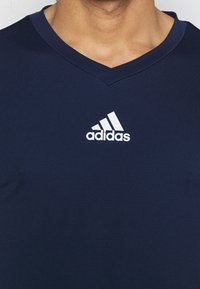 Navy sininen, lyhythihainen urheilupaita, jossa on V-pääntie ja teksturoitu kangas. Paidassa on valkoinen Adidas-logo rinnassa.