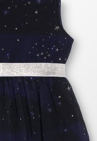 Abito blu scuro con motivo di stelle argentate, presenta una cintura scintillante in argento. Il tessuto è morbido con una texture plissettata nella parte dello skirt.