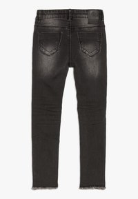 Jeans negros ajustados de mezclilla, con una textura desgastada, dos bolsillos traseros con solapas en ángulo y un dobladillo sin terminar en la parte inferior.