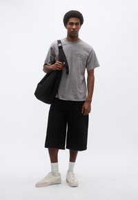 Γκρι βαμβακερό μπλουζάκι, μαύρο σορτς μέχρι το γόνατο, λευκά αθλητικά παπούτσια με μπεζ λεπτομέρειες και μαύρη τσάντα ώμου. Απλό φόντο.