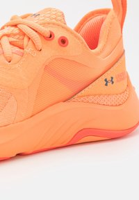 Neon orange idrottssko med en texturerad mesh-övre, släta överlägg och en vadderad sula med en kontrasterande rosa accent.