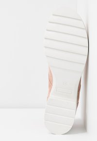 Chaussure en daim rose avec une semelle en caoutchouc blanche présentant des rainures horizontales et un bout arrondi. L'arrière montre une transition lisse vers le dessus.