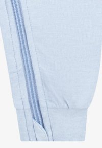 Vaaleansiniset vetoketjulliset jogger-housut, joissa on pehmeä, teksturoitu kangas. Housuissa on näkyvä sivuvetoketju ja kapea nilkkamalli.