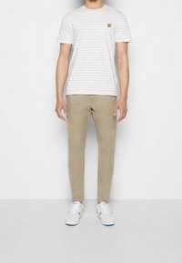 Camiseta blanca a rayas con logo de mariposa amarilla, combinada con pantalones ajustados beige y zapatillas blancas con acentos azules y amarillos.