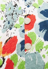 Blommönstrad tyg med ljusblå, röd, grön och svarta accenter, tillsammans med två klara knappar präglade med "RL" på en vit bakgrund.