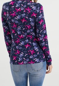 Kvinna som bär en marinblå långärmad tröja med rosa och lila blommönster och ljusblå jeans, sedd bakifrån.