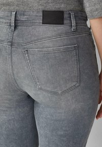 Szare dżinsy z widocznymi tylnymi kieszeniami i szlufkami noszone przez osobę w szarym swetrze.