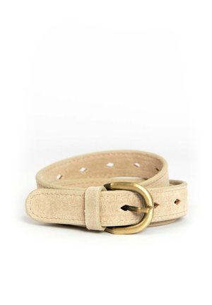 Ceinture en daim beige avec boucle en laiton arrondie, plusieurs trous en forme de losange et bords cousus, enroulée sur un fond blanc.