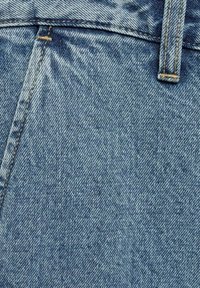 Acercamiento a una tela de denim azul con costura de bolsillo visible, puntadas y detalle del lazo del cinturón.