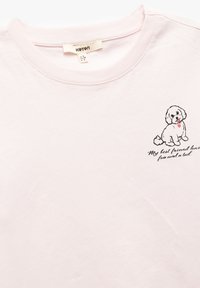 Camiseta de algodón rosa claro con una ilustración contorneada en negro de un perro y texto que dice: "Mi mejor amigo tiene pelaje y cola."