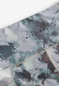 Aktiivspordileggingsid abstraktse sinise ja halli mustriga, valmistatud venivast kangast, nähtava brändi logoga ja lapitehnikaga.