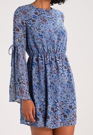 Vestido floral en azul claro con mangas largas y translúcidas, cintura ajustada y una silueta fluida. Presenta una mezcla de pequeñas flores rojas y blancas.
