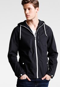 Black hooded jacket in lightweight fabric with white zipper, front pockets, and adjustable drawstrings on the hood. Minimalist design.