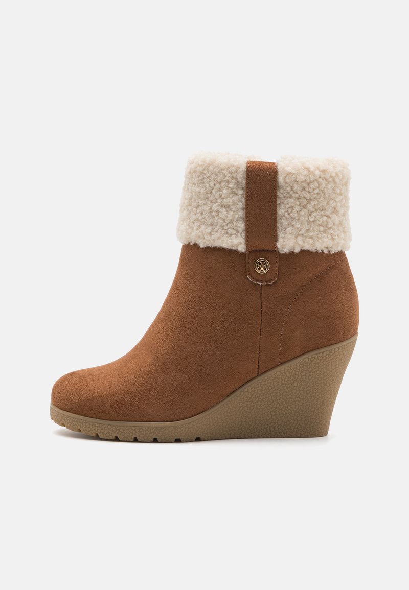 Botim de tornozelo em camurça castanha com punho de pelúcia sintética creme, salto plano e sola de borracha texturizada. Apresenta detalhe de botão lateral.