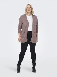 Lys mauve strikket cardigan med åpen front, to frontlommer, ribbestrikkede mansjetter, kombinert med en hvit topp og svarte skinny jeans. Svarte ankelstøvler.