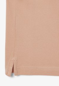 Gros plan sur un tissu texturé couleur pêche avec une fente latérale et une couture visible sur l'ourlet inférieur.