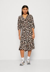 Kjole med leopardmønster, omslagdesign, puffede ermer og flæsekant. Laget av lett stoff. Kombinert med sølvfargede sportssko.