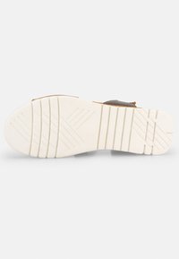 Semelle de sandale avec un fond en caoutchouc blanc texturé et des sangles en cuir brun foncé. Présente des lignes de traction horizontales et diagonales.