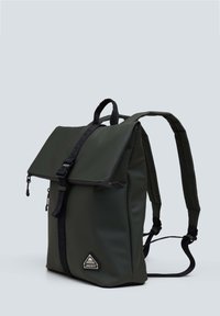 Vihreä vedenpitävä reppu, jossa on taitettava läppä, säädettävät hihnat ja kolmiomainen logo-osa. Sujuva pinta ja minimalistinen muotoilu.