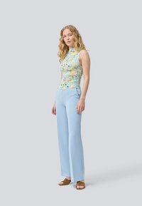 Floral-patterned, sleeveless top with a high neck, paired with light blue, flared trousers. Brown suede slide sandals complete the look.