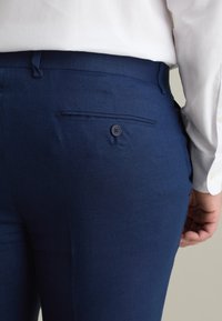 Pantaloni blu navy realizzati in tessuto strutturato, con una tasca posteriore con un solo bottone e un design slim fit.