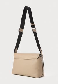 Beige læder crossbody taske med en tekstureret overflade, sort justerbar rem og flaplukning. Har minimal hardware og en strømlinet silhuet.
