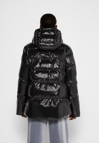 Černá péřová bunda s lesklým, reflexním povrchem. Obsahuje vodorovné prošívané části a velkou, měkkou kapuci.