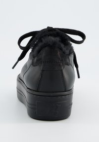 Schwarzer Sneaker mit strukturiertem Lederobermaterial, Kunstpelzakzenten an der Ferse und flachen Schnürsenkeln. Die Sohle ist dick und mit Grip-Mustern versehen.