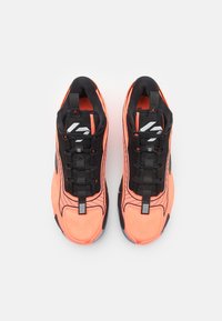 Sportssko i sort og lys koralfarvet, med strukturerede overdele, snørebåndslukning og en mønstret sål med en løkker ved hælen.