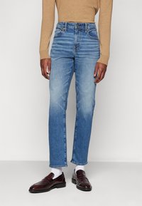 Lyseblå denimjeans med rett snitt, falming nær knærne, kombinert med mørk burgunder loafers og hvite sokker.