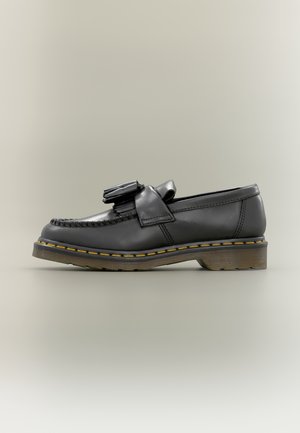 Zwarte leren loafer met kwastjes, gele stiksels langs de zool en dikke rubberen zool, zijaanzicht op een neutrale achtergrond.