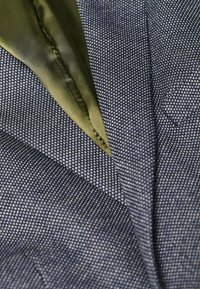 Tessuto blu navy con una sottile trama. Presenta un accento in raso verde che sbircia dal bordo superiore, creando un effetto a strati.