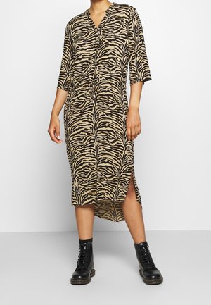 Vestido midi de estampado de cebra en beige y negro, con escote en V, mangas tres cuartos, aberturas laterales y un corte holgado. Se llevan botas de combate negras.