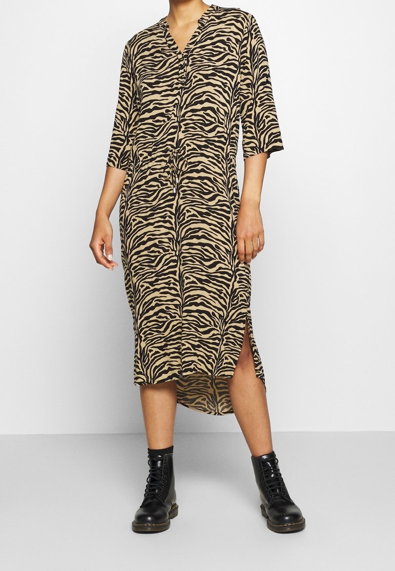 Abito midi a stampa zebra in beige e nero, con scollatura a V, maniche a tre quarti, spacchi laterali e una vestibilità morbida. Indossate con stivali militari neri.