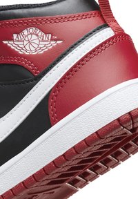 Czarne skórzane sneakersy z czerwonymi akcentami, białą podeszwą środkową i teksturowaną gumową podeszwą. Posiadają logo Air Jordan na pięcie.