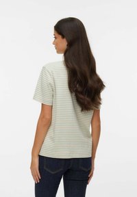 Randig t-shirt i ljusgrönt och vitt, korta ärmar, mjukt bomullstyg, ledig passform, bärs med mörka denimjeans.