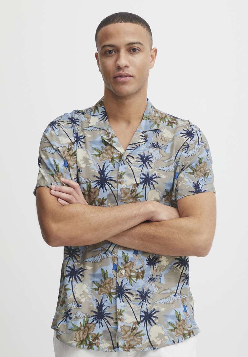 Cămașă cu mânecă scurtă, cu nasturi, având un model tropical în nuanțe de albastru deschis, bej și verde, cu palate de palmier și flori, pe un material texturat.