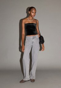 Top negru fără bretele din catifea, blugi largi din denim gri deschis cu accente cu ținte și o geantă texturată neagră. Fundal gri.